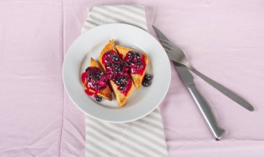 Ev yapımı frenk üzümü reçeli çatal ve bıçak üzerinde parlak koyu kırmızı masa örtüsü ile lezzetli tost ekmeği