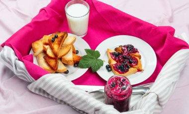 Lezzetli tost ekmeği ev yapımı frenk üzümü reçeli ve parlak kırmızı masa örtüsü üzerinde süt.