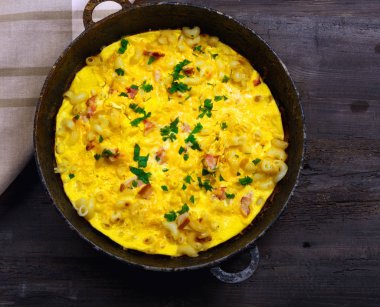 Pastırma, makarna ve Yeşiller eski siyah kızartma tavası vintage ahşap masa arka plan üzerinde tarih ile geleneksel rustik omlet. Kopya alanı