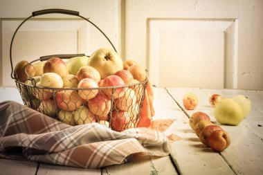 Olgun taze kayısılar ve elmalar dokunmuş metal sepetin içinde odasındaki ahşap masanın üzerinde.