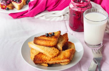 Lezzetli tost ekmeği ev yapımı frenk üzümü reçeli ve parlak kırmızı masa örtüsü üzerinde süt.