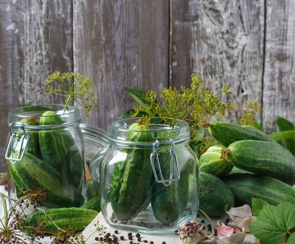 Preserved cucumbers in glass jars with garlic and dill on wooden table