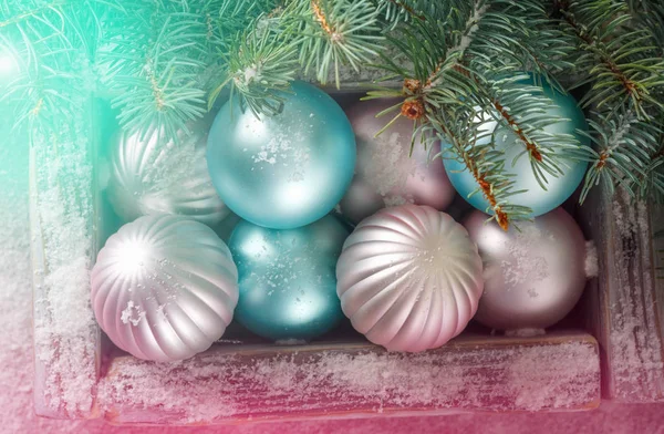緑のモミの枝と明るいライトの背景に美しいピンクとブルー クリスマス ボールと古いヴィンテージ木箱 — ストック写真