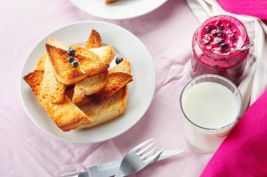Lezzetli tost ekmeği ev yapımı frenk üzümü reçeli ve parlak kırmızı masa örtüsü üzerinde süt.