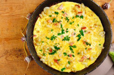 Pastırma, makarna ve Yeşiller eski siyah kızartma tavası vintage ahşap masa arka plan üzerinde tarih ile geleneksel rustik omlet. Kopya alanı