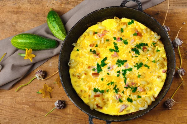 Pastırma, makarna ve Yeşiller eski siyah kızartma tavası vintage ahşap masa arka plan üzerinde tarih ile geleneksel rustik omlet. Kopya alanı