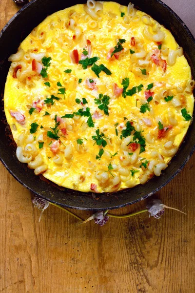 Pastırma, makarna ve Yeşiller eski siyah kızartma tavası vintage ahşap masa arka plan üzerinde tarih ile geleneksel rustik omlet. Kopya alanı