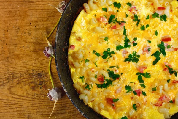 Pastırma, makarna ve Yeşiller eski siyah kızartma tavası vintage ahşap masa arka plan üzerinde tarih ile geleneksel rustik omlet. Kopya alanı