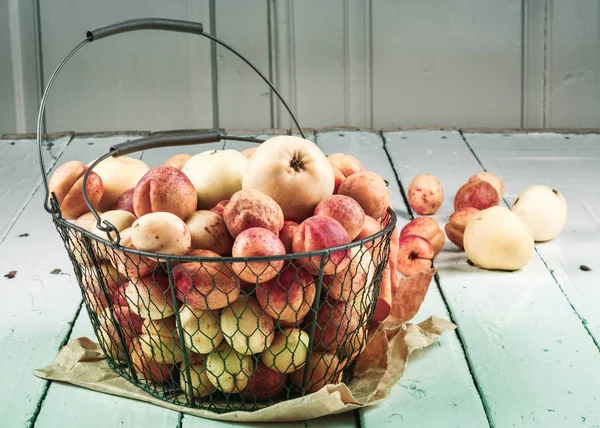 Olgun taze kayısılar ve elmalar dokunmuş metal sepetin içinde odasındaki ahşap masanın üzerinde.