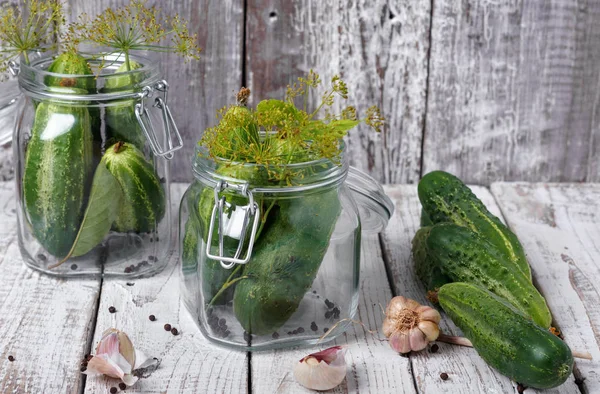 Preserved cucumbers in glass jars with dill and garlic on wooden table