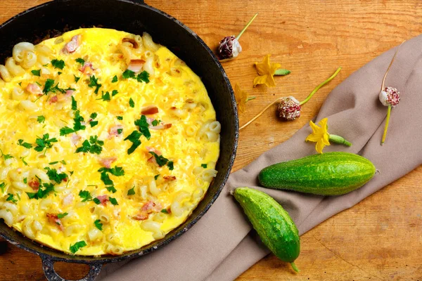 Pastırma, makarna ve Yeşiller eski siyah kızartma tavası vintage ahşap masa arka plan üzerinde tarih ile geleneksel rustik omlet. Kopya alanı