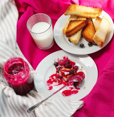 Ev yapımı frenk üzümü lezzetli Tost ekmeğine reçel parlak koyu kırmızı masa örtüsü üzerinde. Kahvaltı kalıntıları
