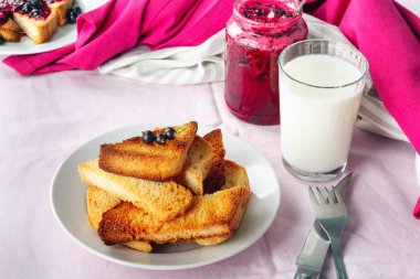 Lezzetli tost ekmeği ev yapımı frenk üzümü reçeli ve parlak kırmızı masa örtüsü üzerinde süt.