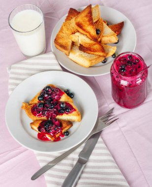 Lezzetli tost ekmeği ev yapımı frenk üzümü reçeli ve parlak kırmızı masa örtüsü üzerinde süt.