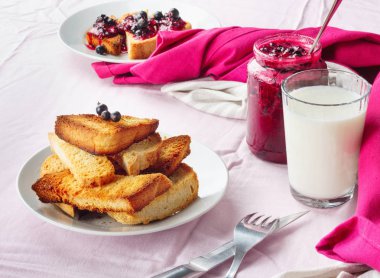 Lezzetli tost ekmeği ev yapımı frenk üzümü reçeli ve parlak kırmızı masa örtüsü üzerinde süt.