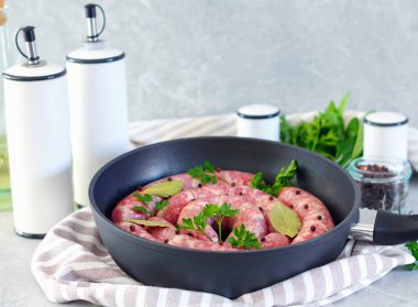 Lezzetli rustik çiğ et sosisleri tavada, defne yaprağı ve mutfakta taze otlar ile