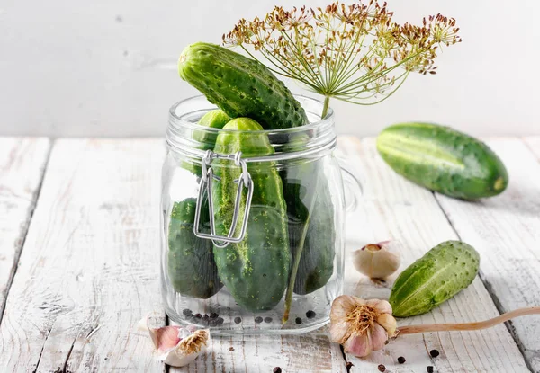 Preserved cucumbers in glass jars with dill, pepper and garlic on wooden table