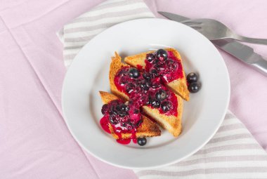 Ev yapımı frenk üzümü reçeli çatal ve bıçak üzerinde parlak koyu kırmızı masa örtüsü ile lezzetli tost ekmeği