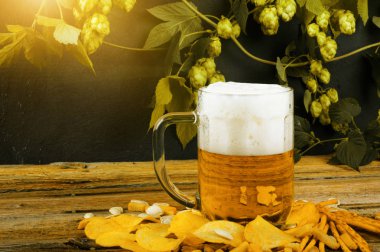 Kraker ve patates kızartması ahşap masa ve şubeler ile karanlık duvara olgun şerbetçiotu ile soğuk taze altın bira cam kupa