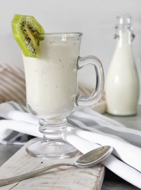 Yoğurt veya süt cam, havlu ile beyaz ahşap zemin üzerinde yeme sağlıklı ile taze karıştırılmış kivi protein güler yüzlü