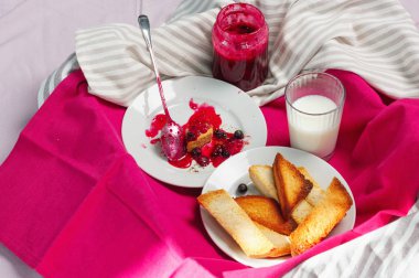 Ev yapımı frenk üzümü lezzetli Tost ekmeğine reçel parlak koyu kırmızı masa örtüsü üzerinde. Kahvaltı kalıntıları