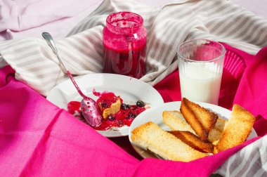 Ev yapımı frenk üzümü lezzetli Tost ekmeğine reçel parlak koyu kırmızı masa örtüsü üzerinde. Kahvaltı kalıntıları