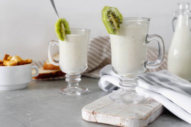 Yoğurt veya süt cam, havlu ile beyaz ahşap zemin üzerinde yeme sağlıklı ile taze karıştırılmış kivi protein güler yüzlü