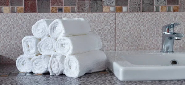 Modern banyodaki seramik tezgahta bir yığın temiz beyaz havlu.