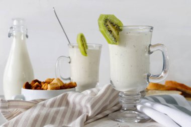 Yoğurt veya süt cam, havlu ile beyaz ahşap zemin üzerinde yeme sağlıklı ile taze karıştırılmış kivi protein güler yüzlü