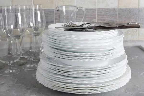 Stack of clean plates with forks, knives and glasses for serving on stone table near the sink