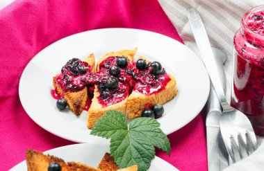 Ev yapımı frenk üzümü reçeli çatal ve bıçak üzerinde parlak koyu kırmızı masa örtüsü ile lezzetli tost ekmeği