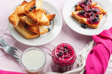 Lezzetli tost ekmeği ev yapımı frenk üzümü reçeli ve parlak kırmızı masa örtüsü üzerinde süt.