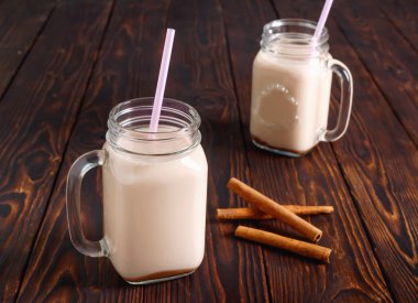 İki cam bardak sıcak kakao rustik ahşap masa üzerinde süt, tarçın ve saman tuplü.
