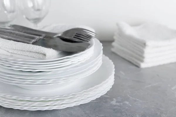 Stapel sauberer Teller mit Gabeln, Messern und Gläsern zum Servieren auf Steintischen — Stockfoto