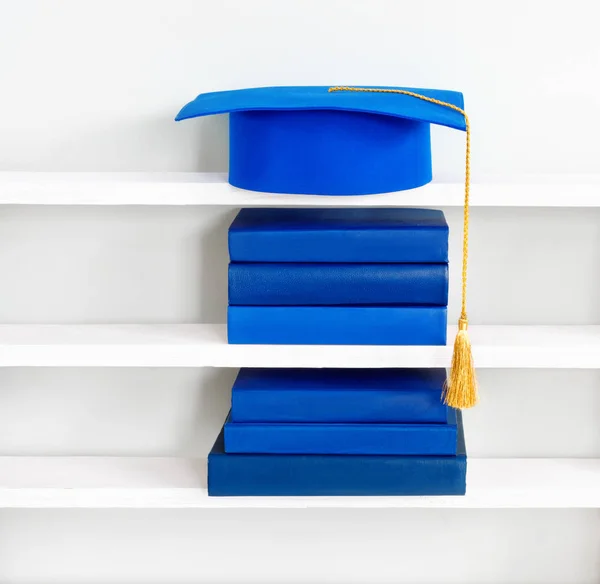 Graduación mortero azul en la parte superior de la pila de libros en el estante de madera — Foto de Stock