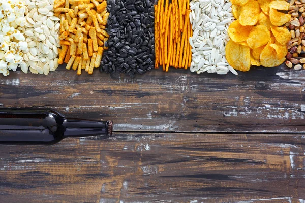 Chips, Cracker, Samen, Nüsse und eine Flasche frisches kaltes Bier auf dem Holztisch — Stockfoto