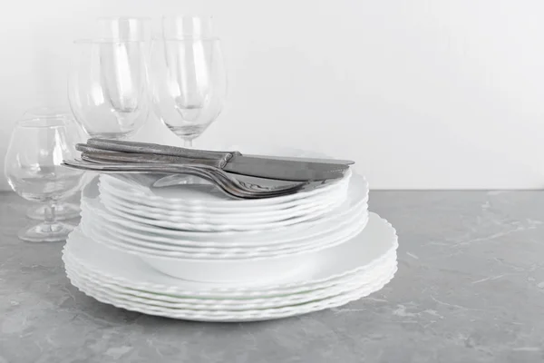 Stack of clean plates with forks, knives and glasses for serving