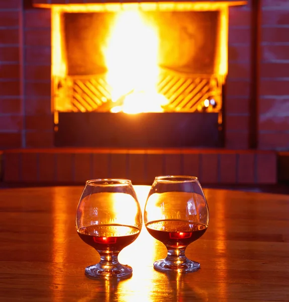 Twee glazen Cognac op de oude bakstenen open haard met felle vuur — Stockfoto