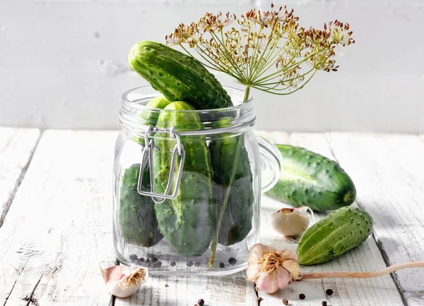 Preserved cucumbers in glass jars with dill, pepper and garlic on table