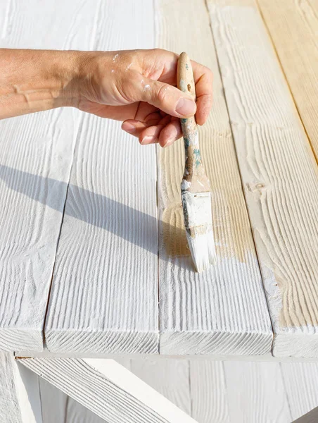 Worker painting white wooden furniture outdoor.