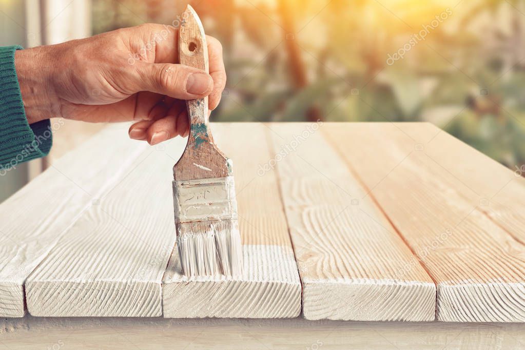 Worker painting white wooden furniture outdoor. 