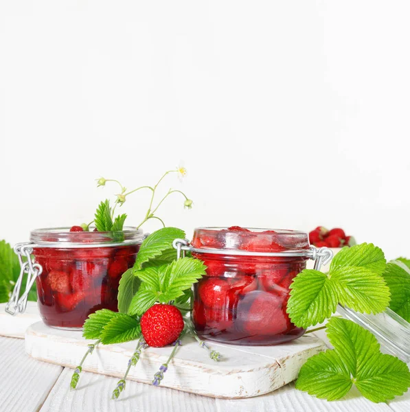 Lahodná jahodová marmeláda v tradiční skleněné sklenici na bílém dřevěném pozadí — Stock fotografie
