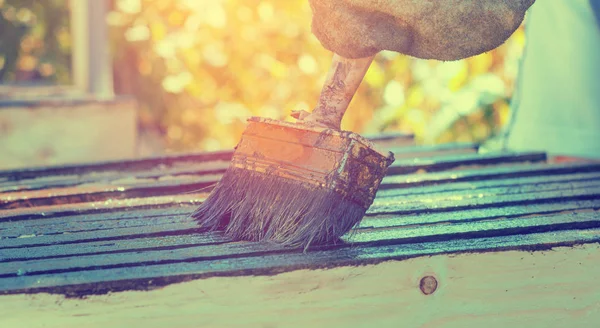 Работник в старой перчатке занимается покраской досок для украшения дома — стоковое фото