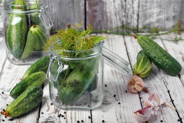 Preserved cucumbers in glass jars with garlic and dill on table