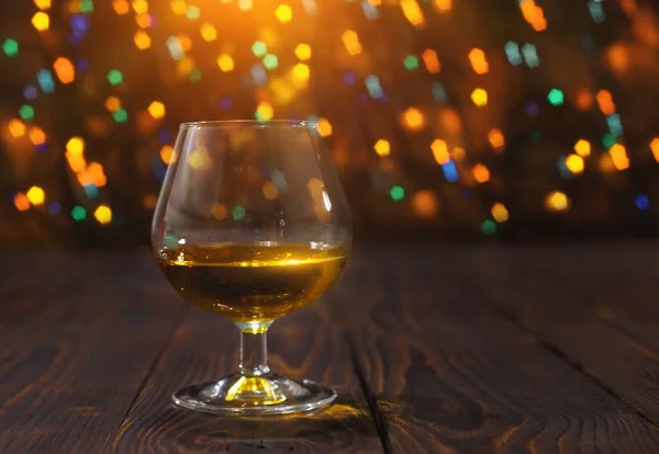 Glass of whiskey or brandy on wooden table on bright glowing background — Stock Photo, Image