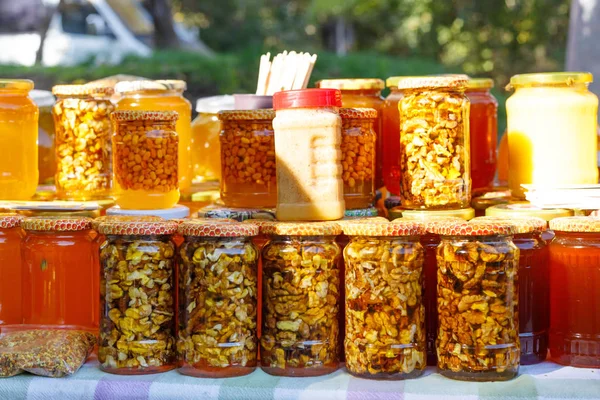 Frascos y palitos de miel con miel natural en el estante en feria. Venta de miel natural en el mercado exterior . — Foto de Stock