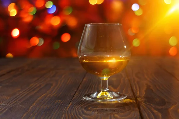 Glass of whiskey or brandy on wooden table on bright glowing background — Stock Photo, Image
