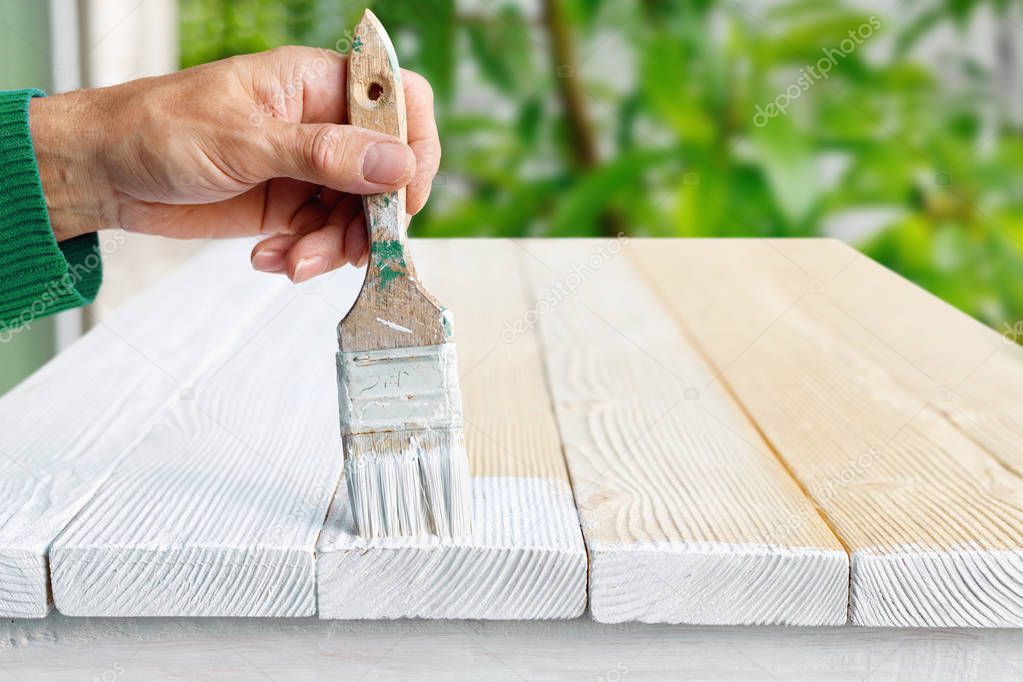 Worker painting white wooden furniture outdoor. 