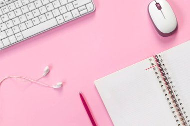 Dizüstü bilgisayarı, bilgisayarı, kulaklığı ve pembe kağıtta bilgisayar faresi olan beyaz ofis masasının üst görüntüsü.