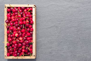 Yaz yeşilliğinin arka planında, gri taştan tezgahta taze kiraz çileği hasadı..